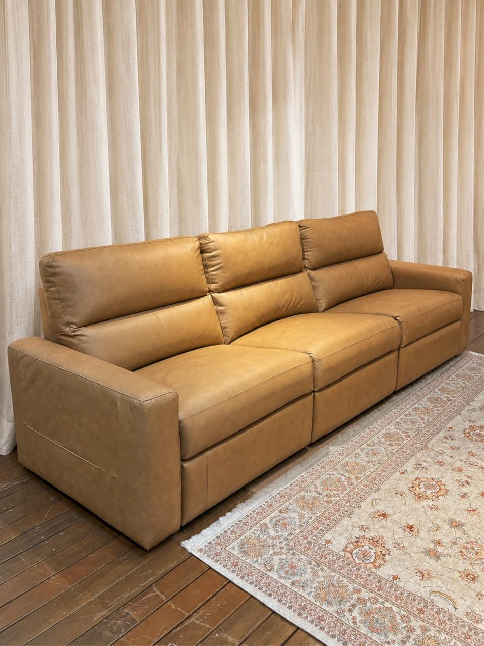 Sofá de couro caramelo em sala de estar decorada pela Nandi Decorações, com cortinas de linho e tapete clássico