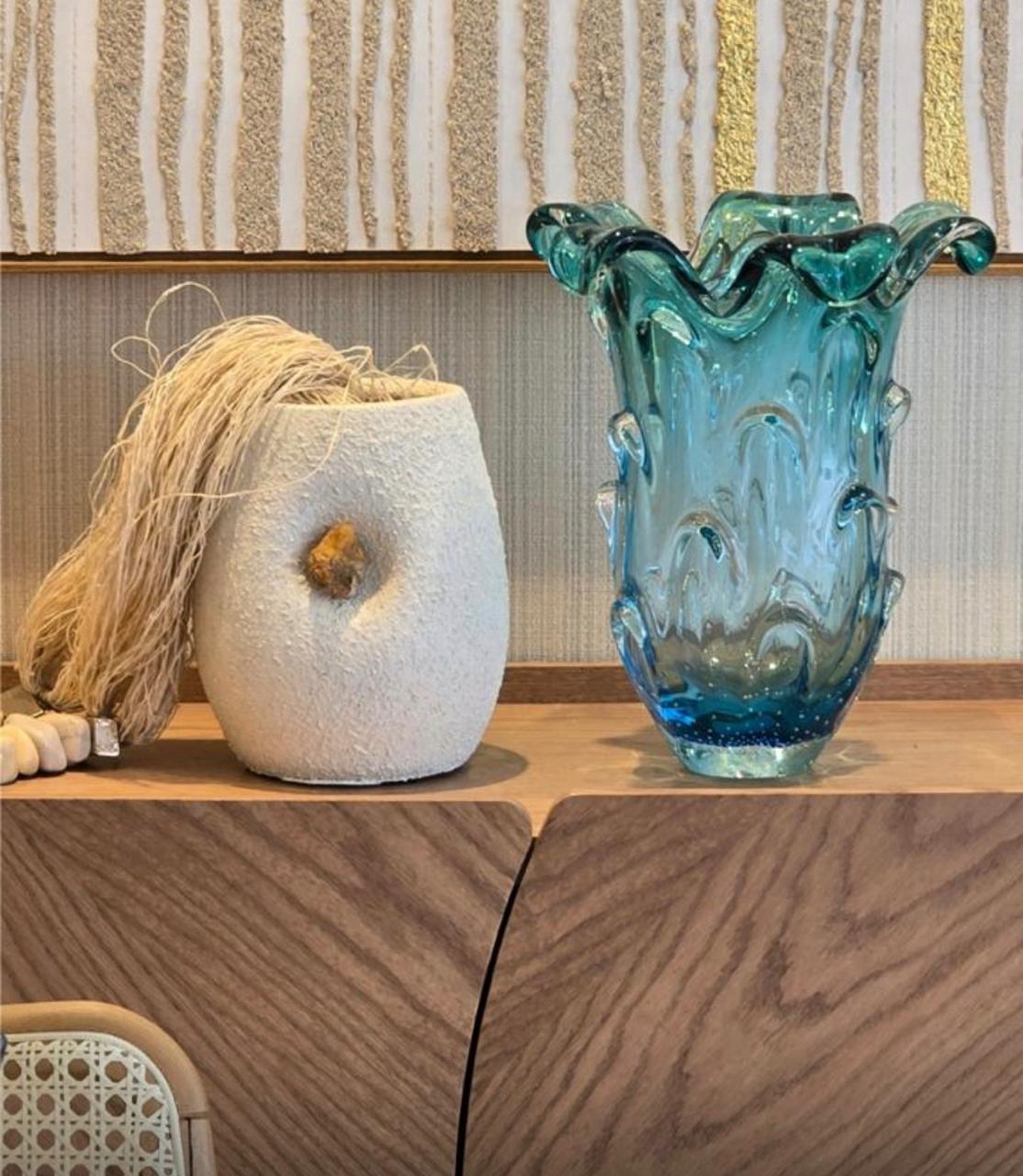 Vaso de vidro azul e vaso texturizado em fibra natural sobre aparador de madeira
