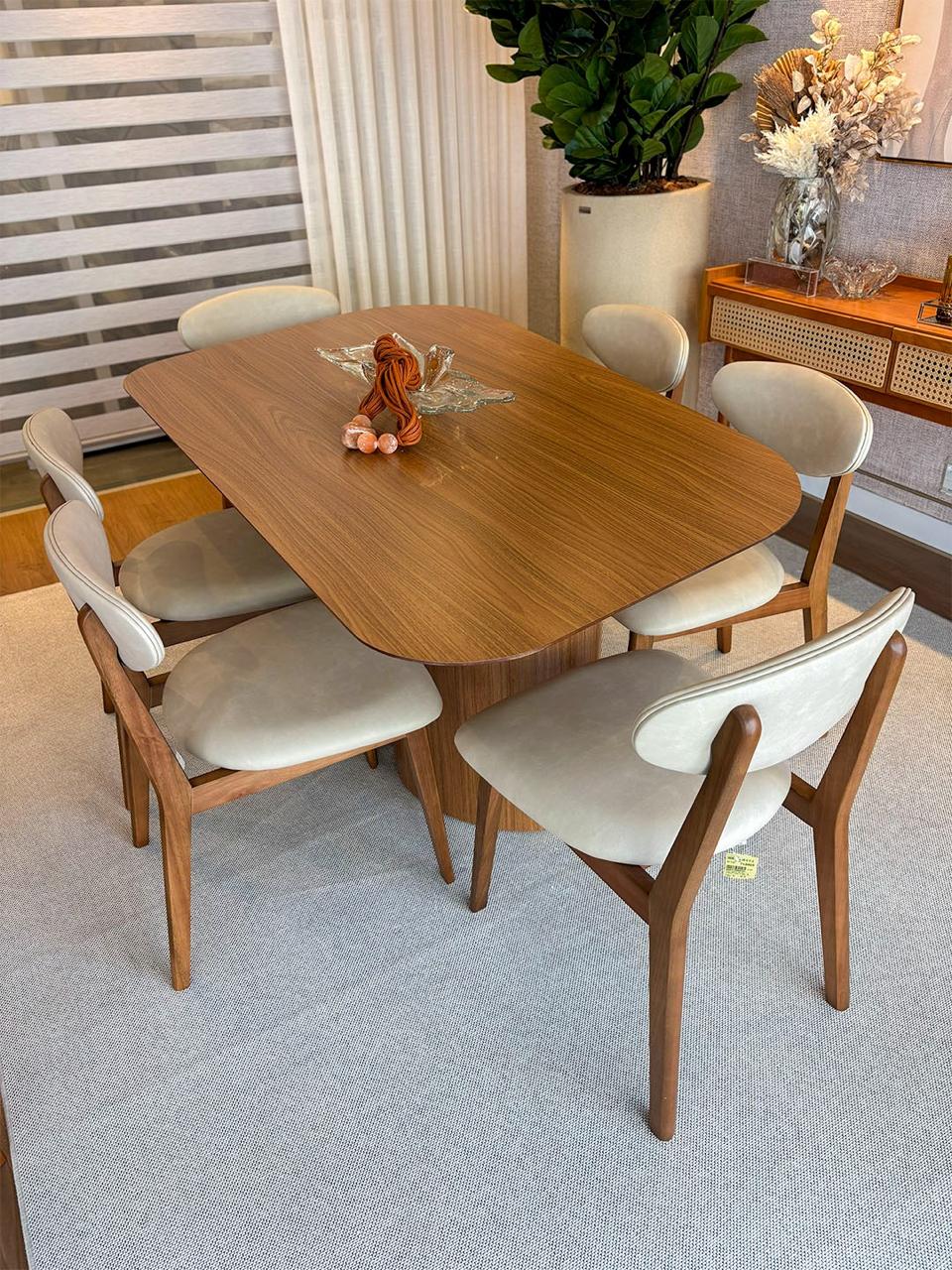 Sala de jantar com mesa oval de madeira nogueira, seis cadeiras estofadas claras e aparador decorado